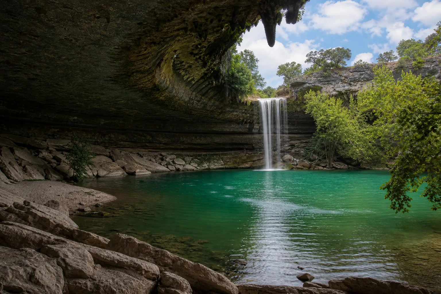 Hamilton Pool Preserve wide view of the collapsed grotto, jade pool, and hamilton creek dropping from the overhanging edwards limestone rim.