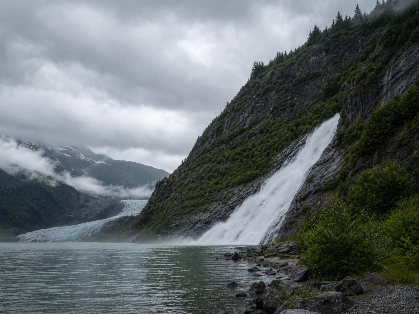 Nugget Falls framed by Mendenhall Lake, dark Coast Mountains cliffs, and low marine clouds